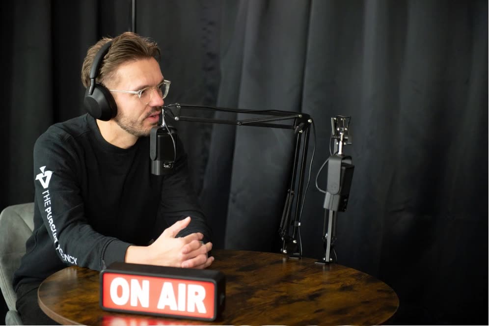 A presenter in headphones speaking into a boom-arm microphone at the studio table in the Pursuit studio, Swindon